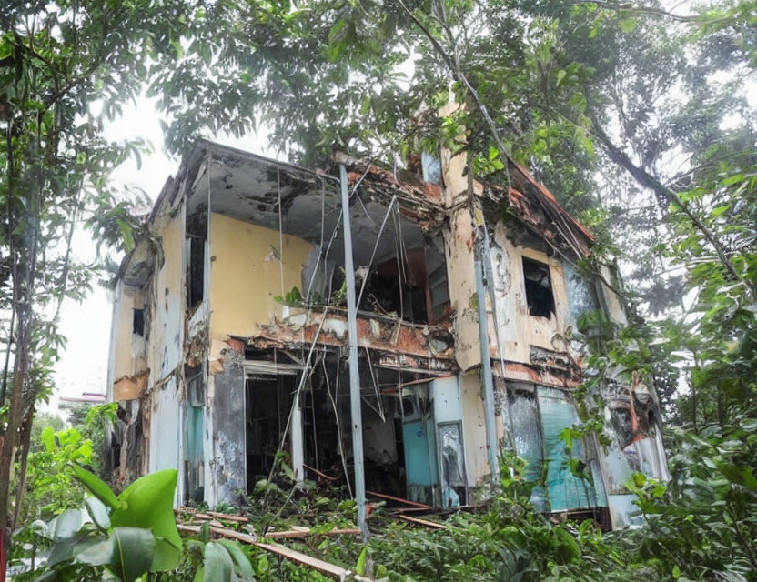 Abandoned two-story building with structural damage and overgrown vegetation in a lush forest