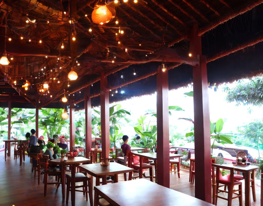 Rustic restaurant with wooden tables, hanging lanterns, and lush greenery view