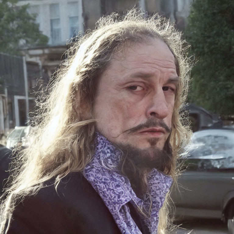 Bearded man with long curly hair in patterned shirt, urban background