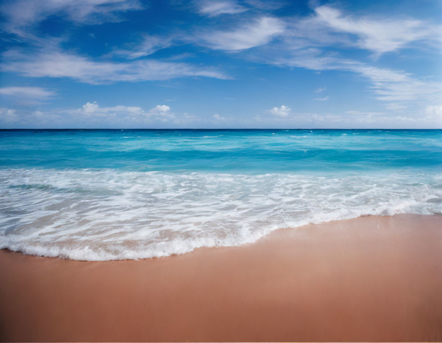 Sandy beach meeting turquoise ocean under cloudy sky