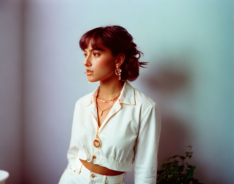 Short-haired woman in white shirt with golden accessories on blue backdrop