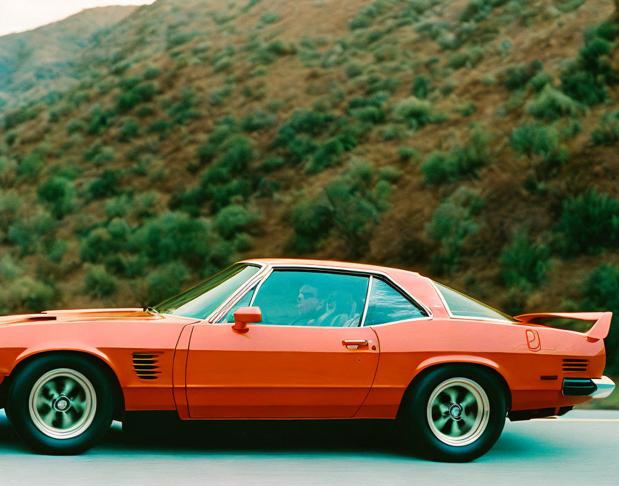 Classic Red Sports Car Driving on Road with Green Hills