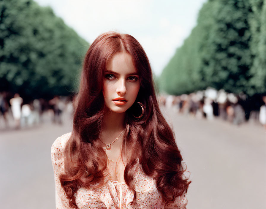 Woman with auburn hair and blue eyes on tree-lined path