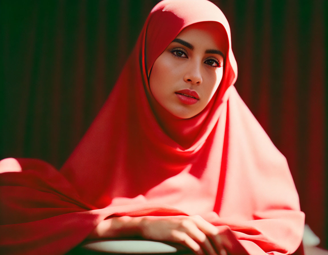 Contemplative woman in red hijab on greenish striped background