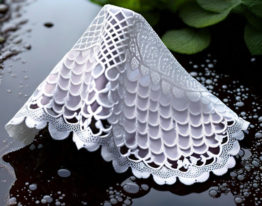 Intricate white lace fabric with water droplets on reflective surface