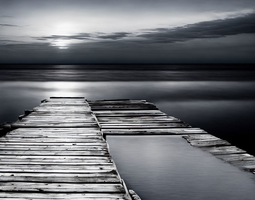 Monochrome weathered wooden pier under cloudy sky and sun