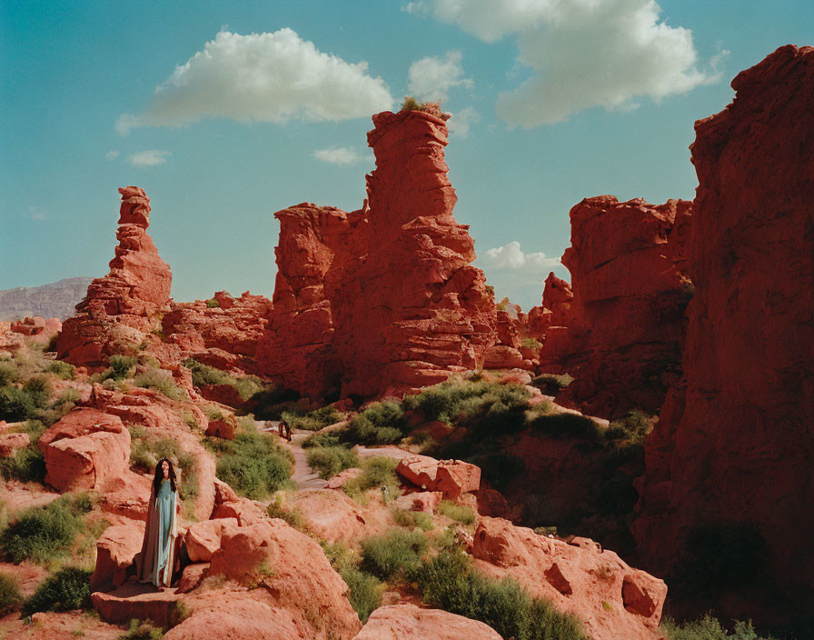 Person standing among towering red rock formations under blue sky