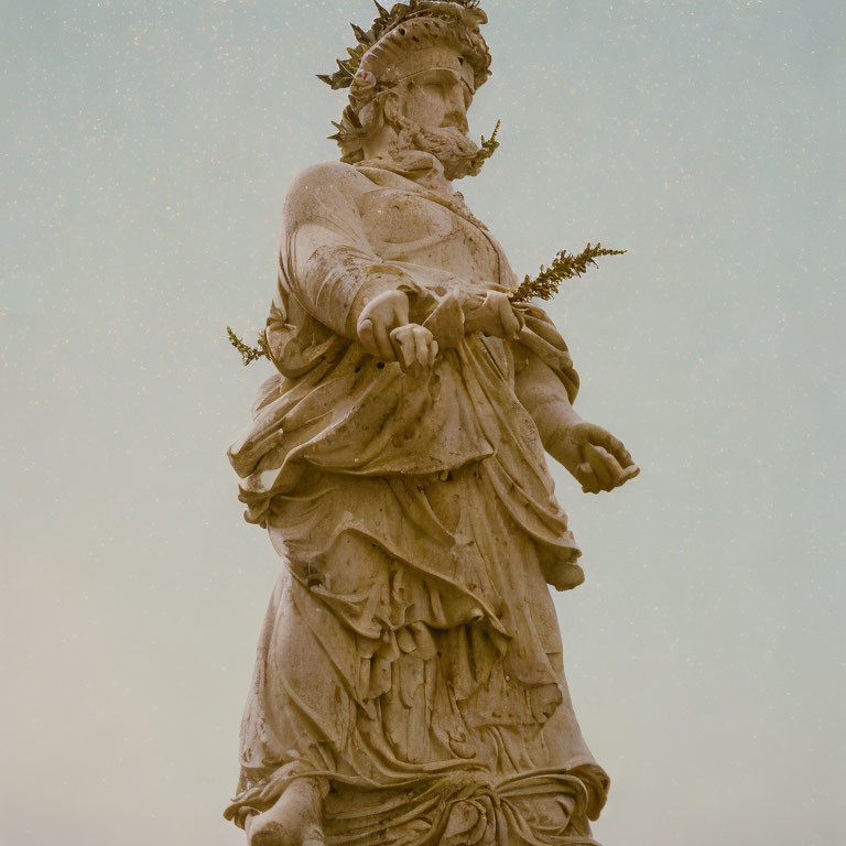 Stone statue of robed figure with crown and laurel branch against pale sky