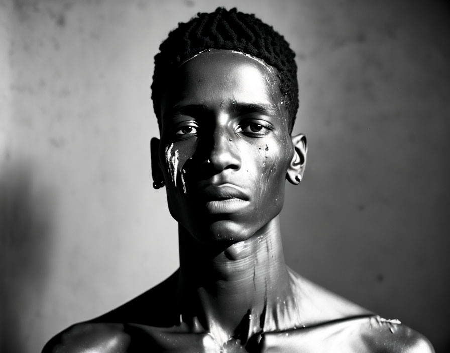 Monochrome portrait of young man with distinct hair texture and paint drips on face, against dark backdrop