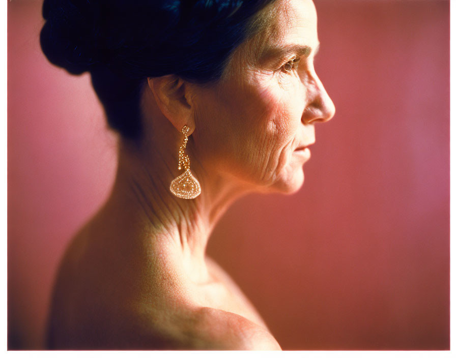 Mature woman with updo hair and teardrop earring on soft pink background