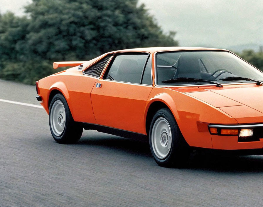 Vintage orange sports car with pop-up headlights in motion on road