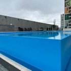 Two leaping dolphins in outdoor pool with buildings.