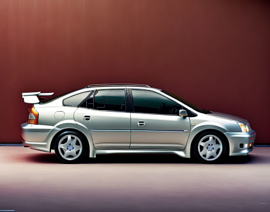 Silver sedan with rear spoiler, tinted windows, and five-spoke wheels on maroon background