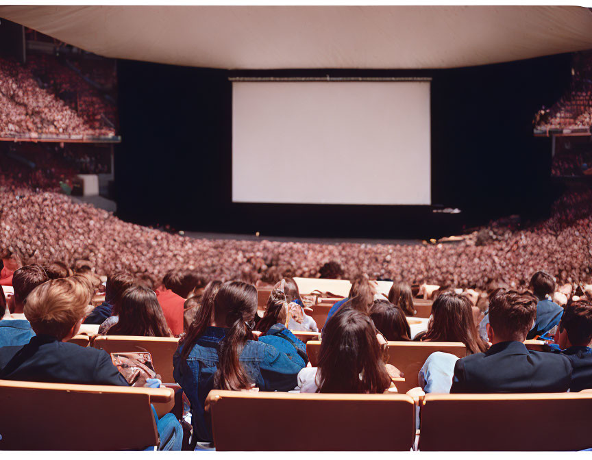 Indoor amphitheater with red seats and large screen.