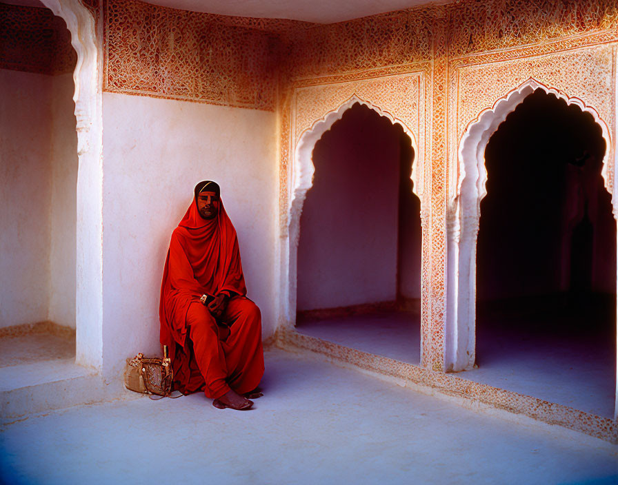 Person in Red Garment Sitting Against Pink Wall in Ornate Archway