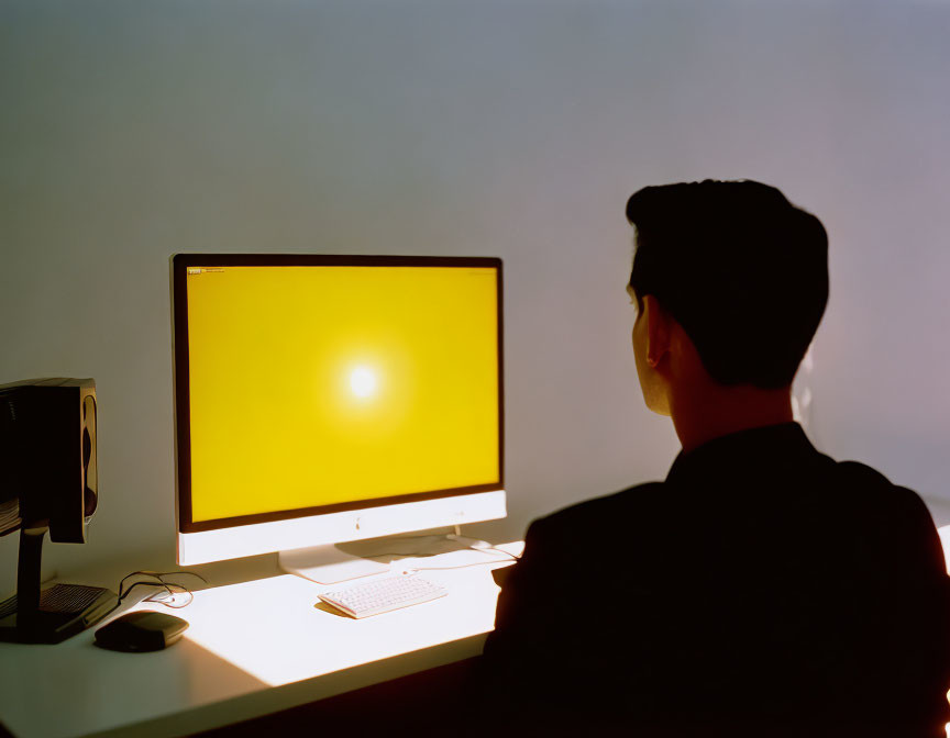 Silhouette profile of person at computer with bright yellow screen