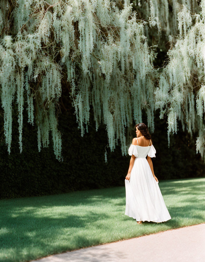 Woman in white off-shoulder dress under willow branches in garden