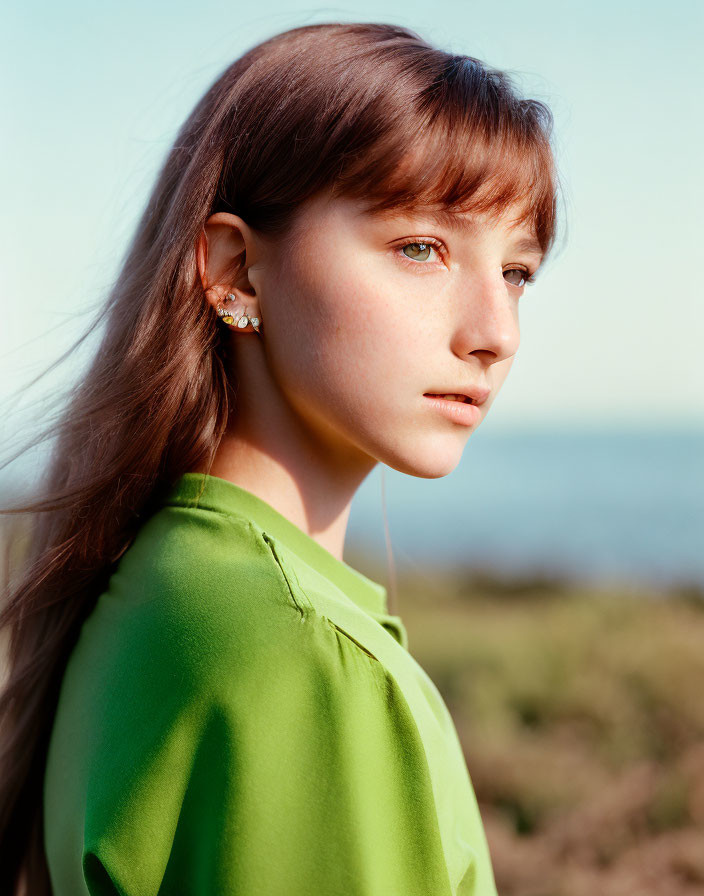 Brown-haired woman in green top gazes at calm sea and sky