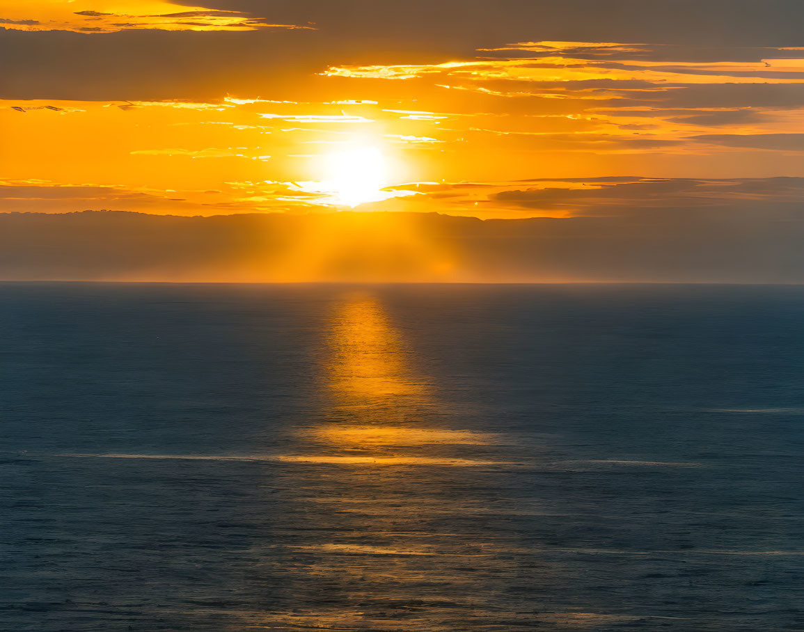 Golden sunset over ocean with clouds and reflection.