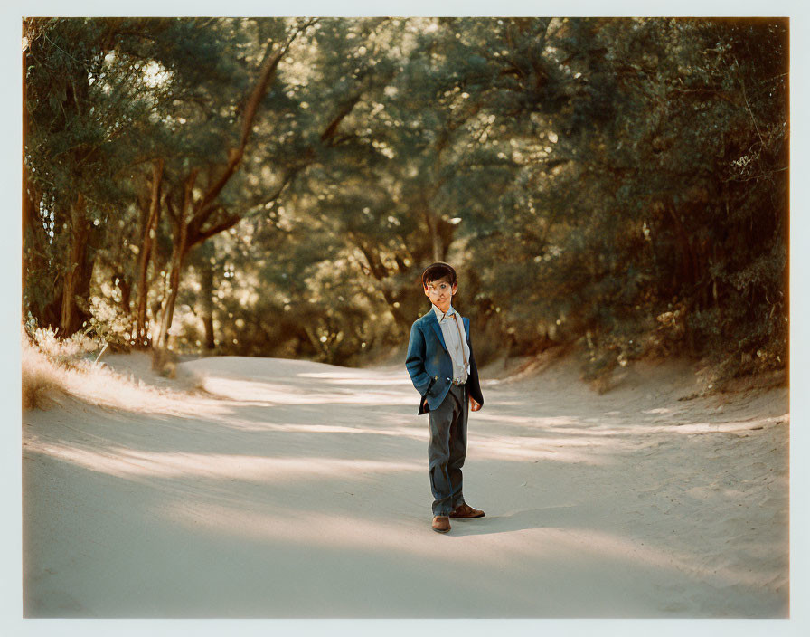 Child in suit standing on sandy path in sunlit forest