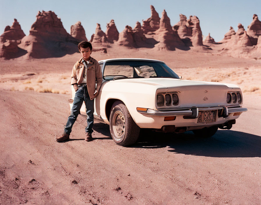 Young boy next to white classic car on desert road with rock formations