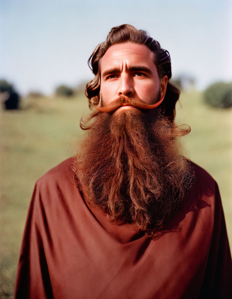 Man with long beard and hair in brown shirt in field under clear blue sky