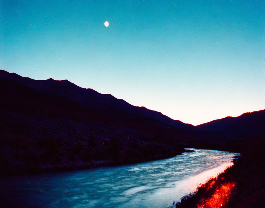 Serene river at twilight with glowing moon and mountain silhouettes