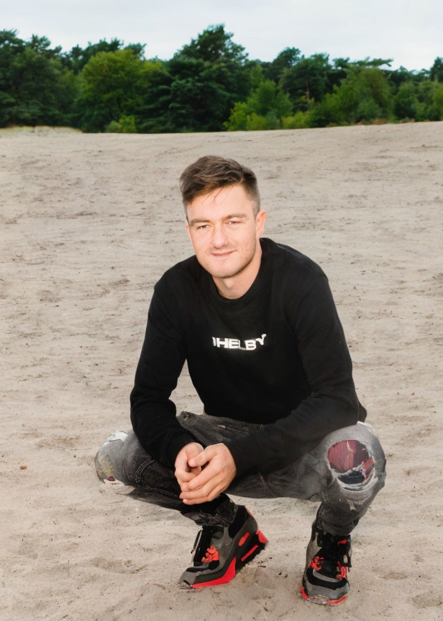 Man in Black Sweatshirt Crouching on Sandy Ground