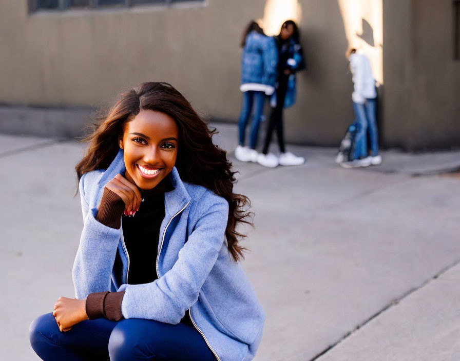 Woman smiling while crouching, people chatting in background on sunny day