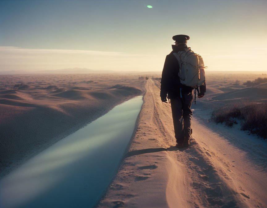 Desert sunset: Solitary figure by narrow water canal