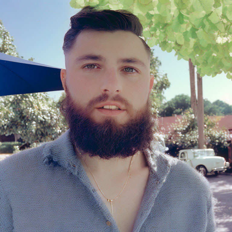 Bearded man in cardigan under tree canopy with vintage car