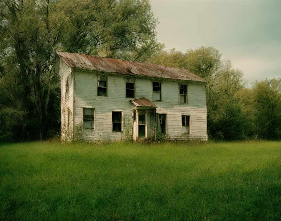 Abandoned two-story house with peeled white paint in overgrown surroundings