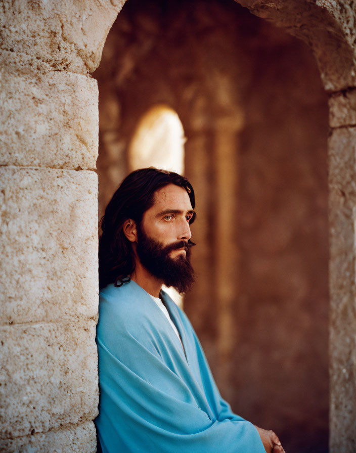 Bearded man in blue robe leans against stone archway