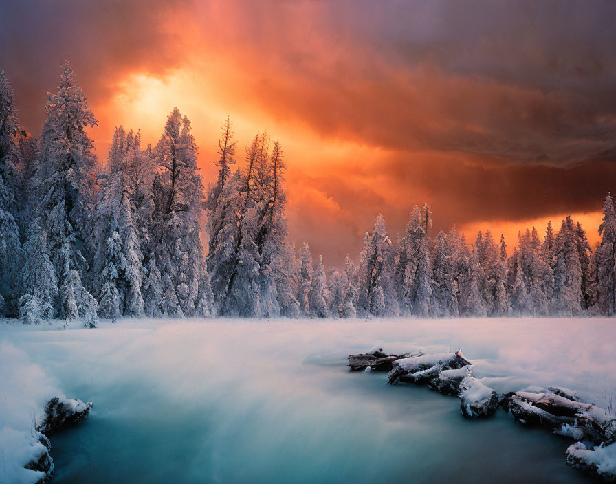 Snow-covered trees, flowing river, dramatic orange and red sky in winter landscape