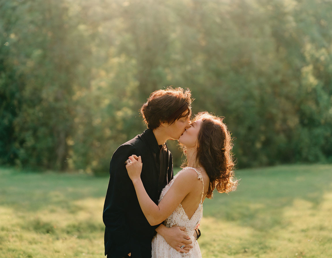 Couple kissing in sunlit field with trees.