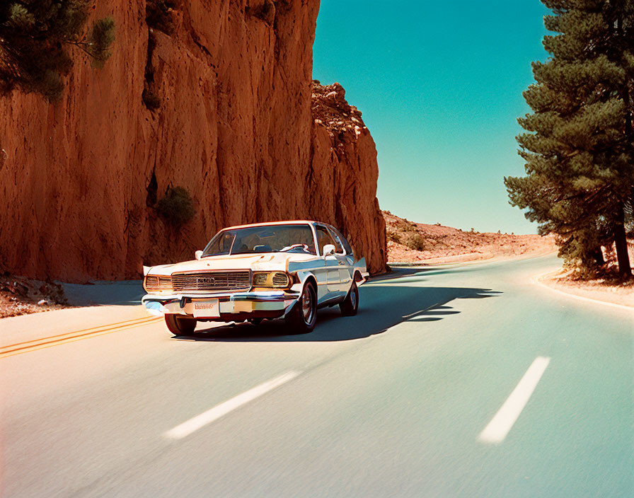 Classic Car Driving Through Rocky Canyon with Pine Trees under Clear Blue Sky