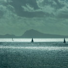 Vintage sailing ships on calm sea under hazy golden sky.