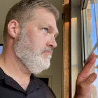 Grey-haired man with beard smiling next to abstract paint splash on window