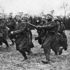 Vintage black-and-white photo of soldiers in early 20th-century military uniforms marching and riding horses.