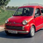 Vintage Red Car Driving on Road Amid Lush Greenery