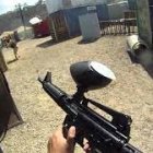 Players in combat gear aiming paintball guns in outdoor field.