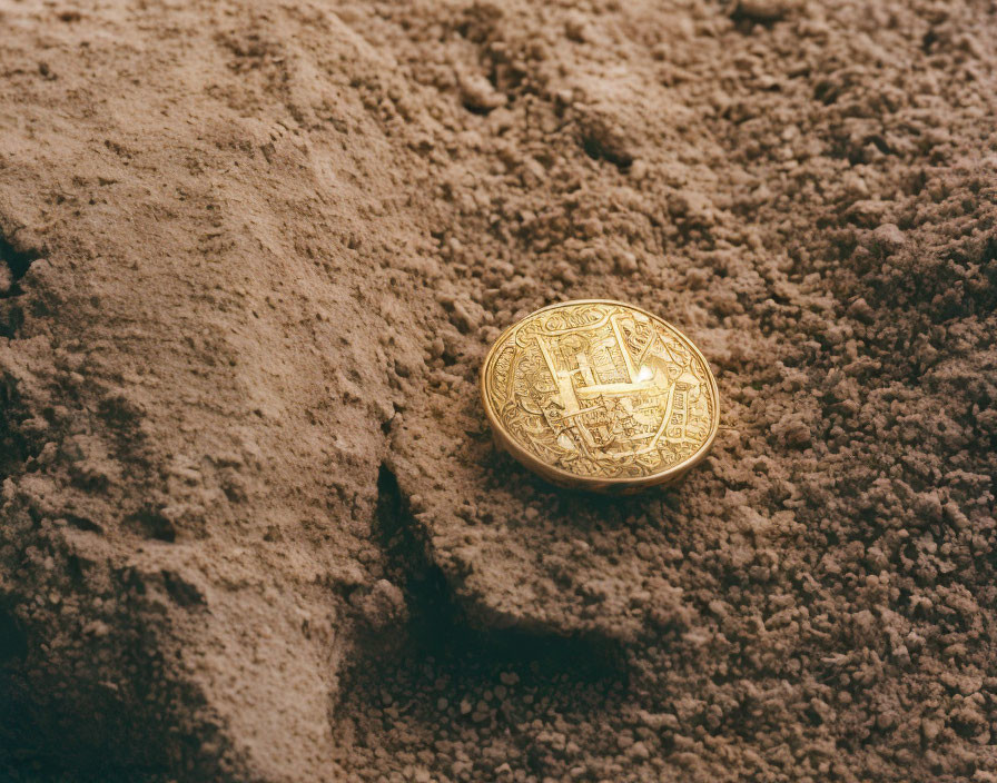 Golden Bitcoin symbol coin partially buried in sand with shadow