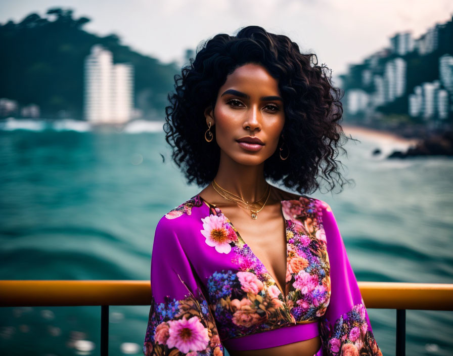 Curly-haired woman in floral dress by coastal cityscape.