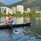 Rowers in double sculls boat on calm lake with white building and blue skies