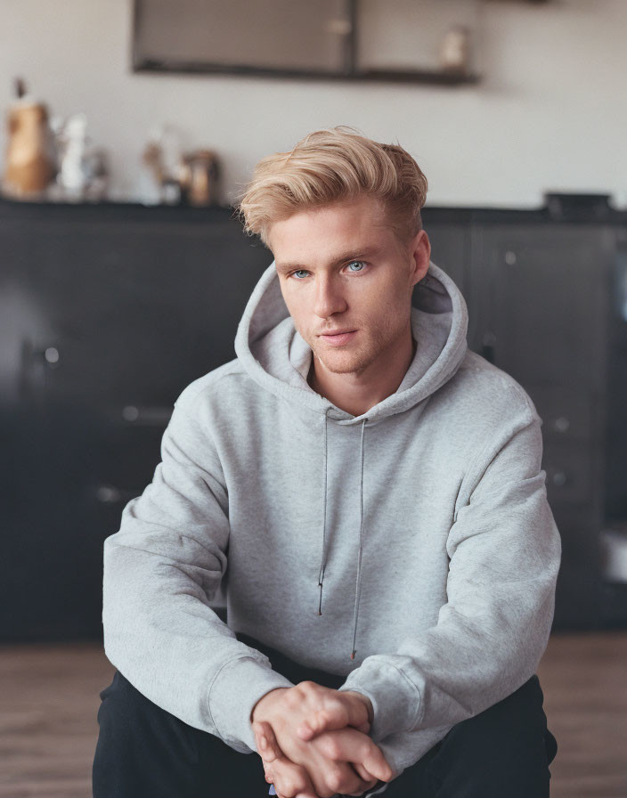 Blond Man in Gray Hoodie with Blue Eyes Sitting Intently