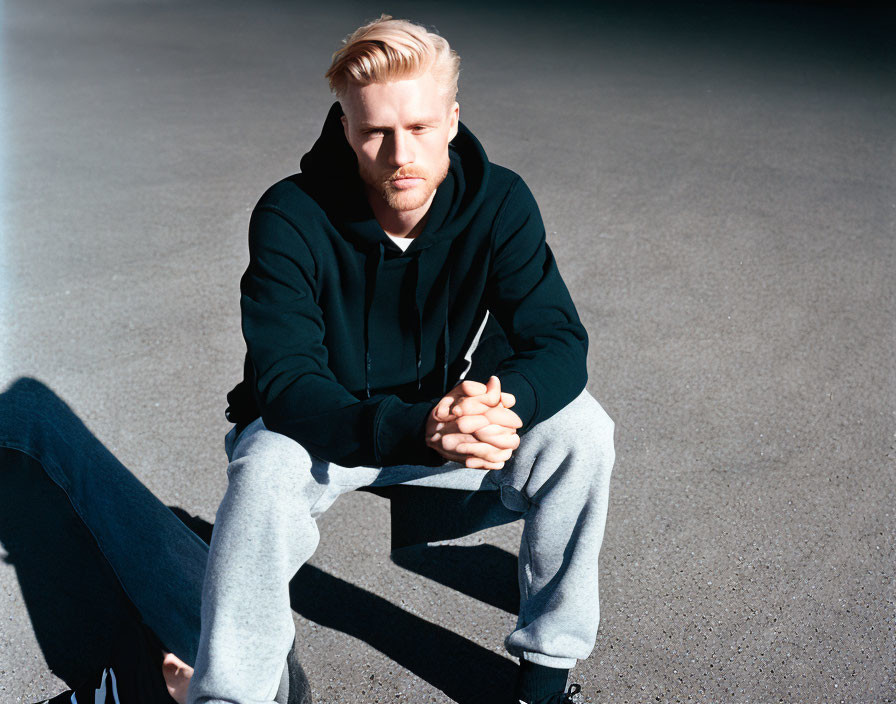 Blond man in black hoodie squats outdoors