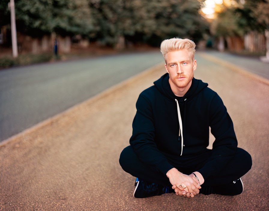 Blond man in black hoodie sitting on empty road