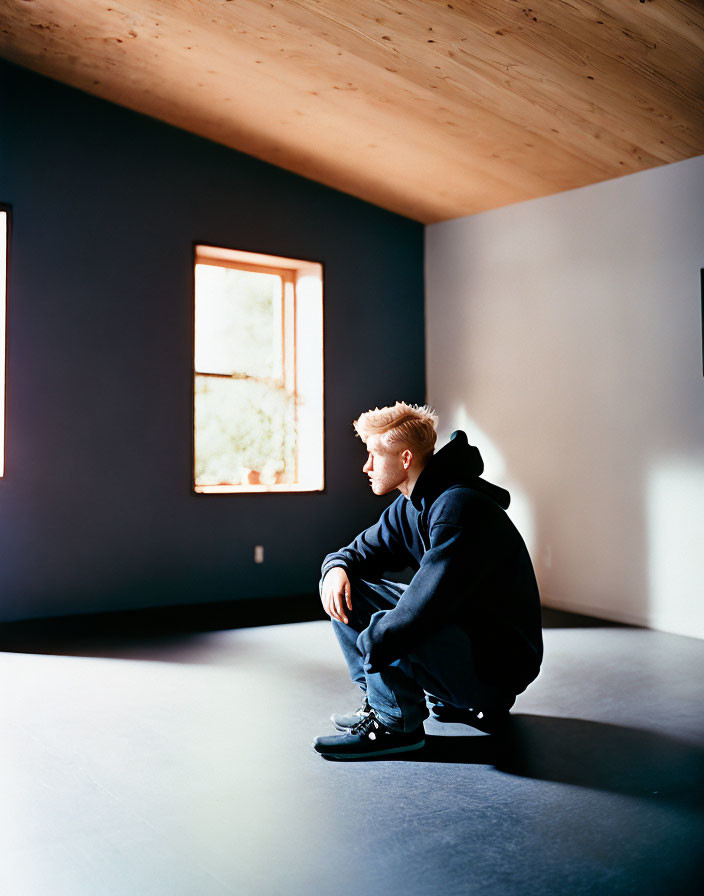 Blond-Haired Person Sitting by Window in Dark Room