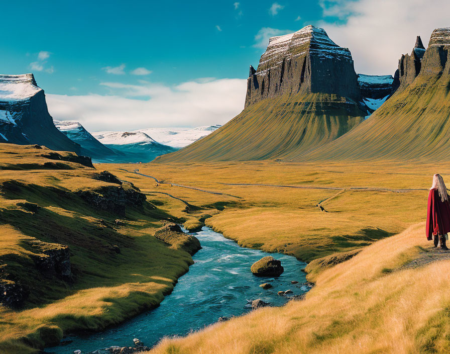 Person in Red Cloak Walking in Lush Green Valley with Snow-Capped Mountains