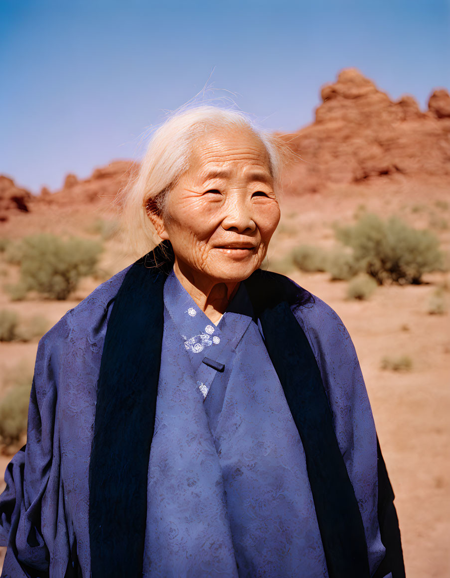 Elderly woman in blue traditional outfit in rocky desert setting